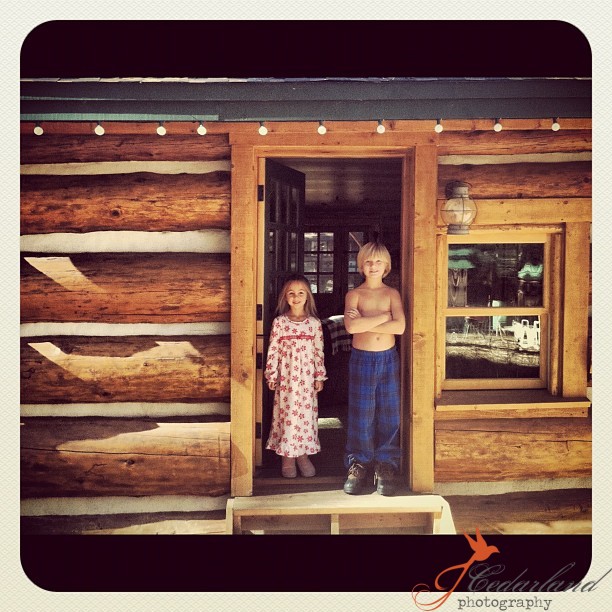 girl and boy in door of log cabin