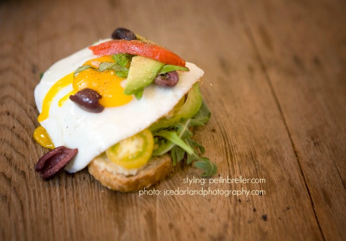 hummus, fresh greens, tomatoes, avocado, bell peppers, olive sandwich topped with fried egg